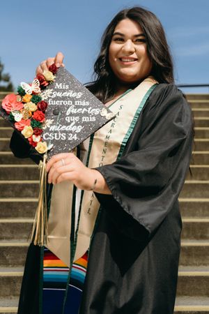 Smiling graduate holds decorated cap reading inspirational Spanish quote at CSUS 2024.