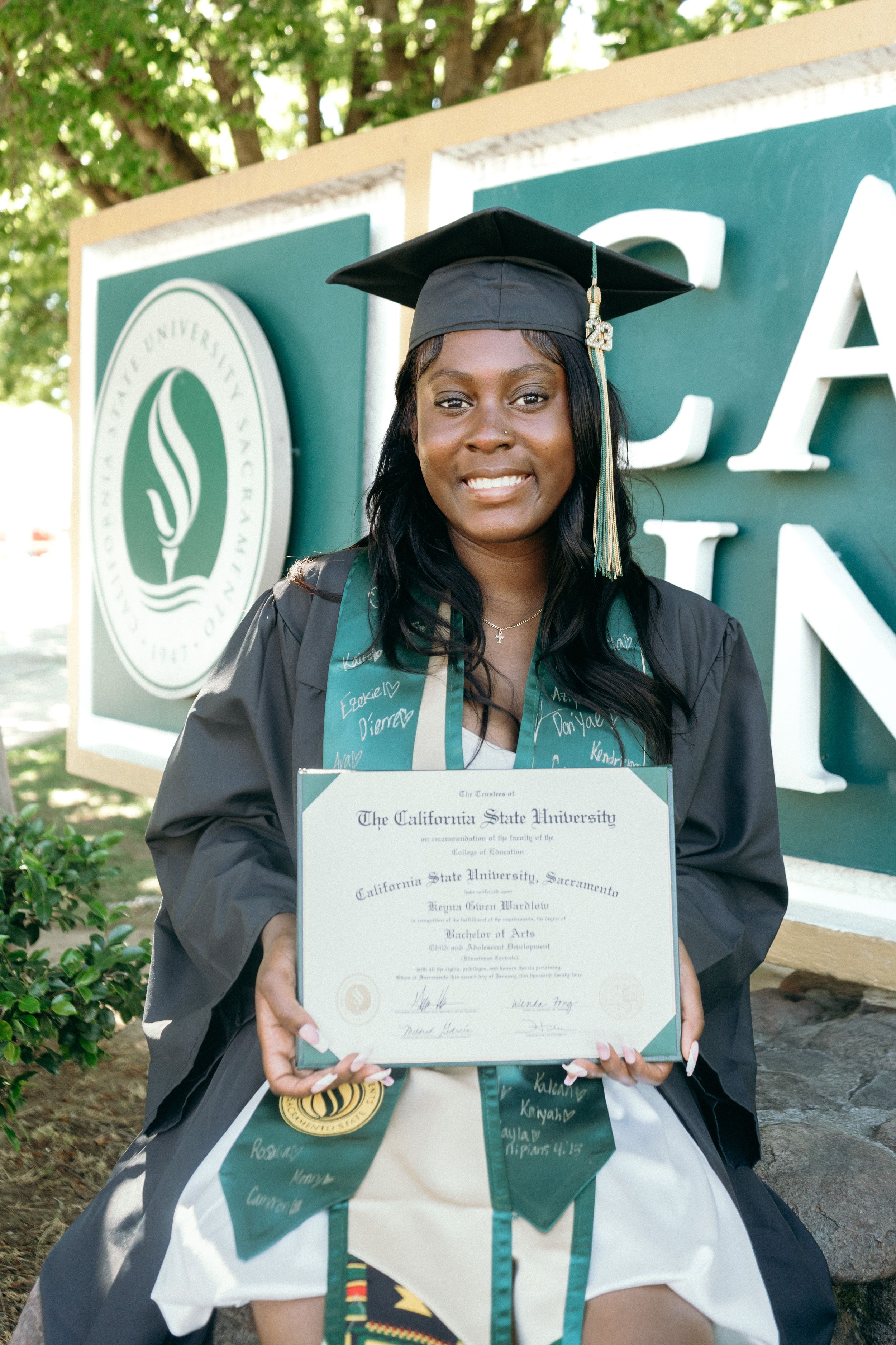 Proud graduate holds Cal State University Sacramento Bachelor of Arts diploma in cap and gown.