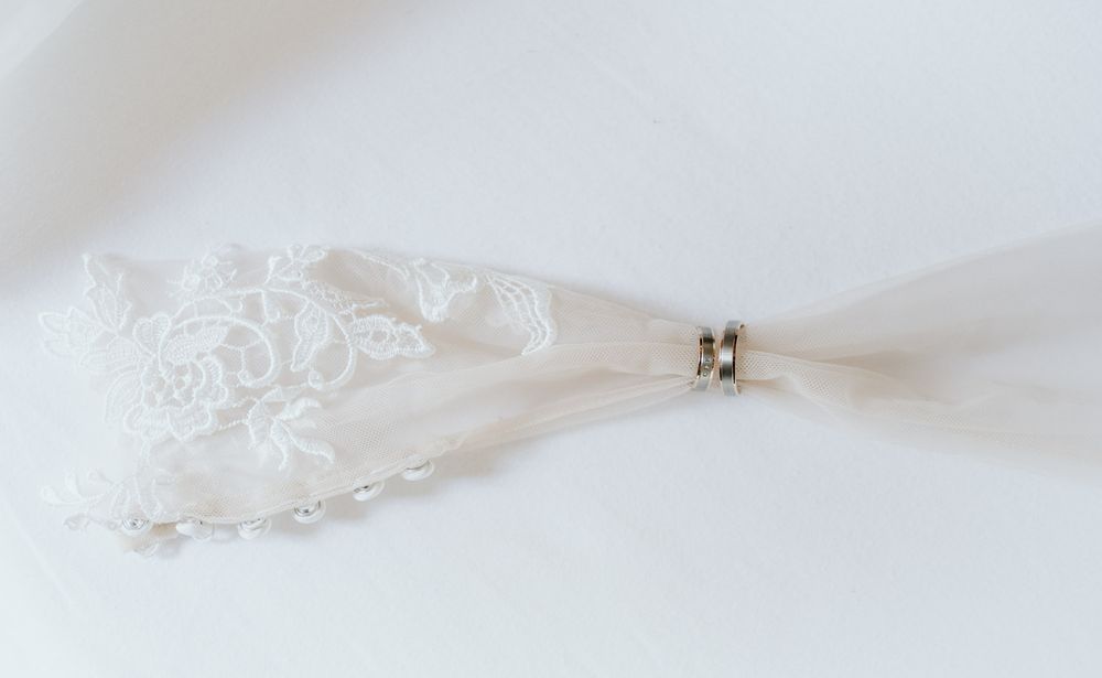 Delicate white lace bridal veil detail with pearl and crystal hair accessory on white background.