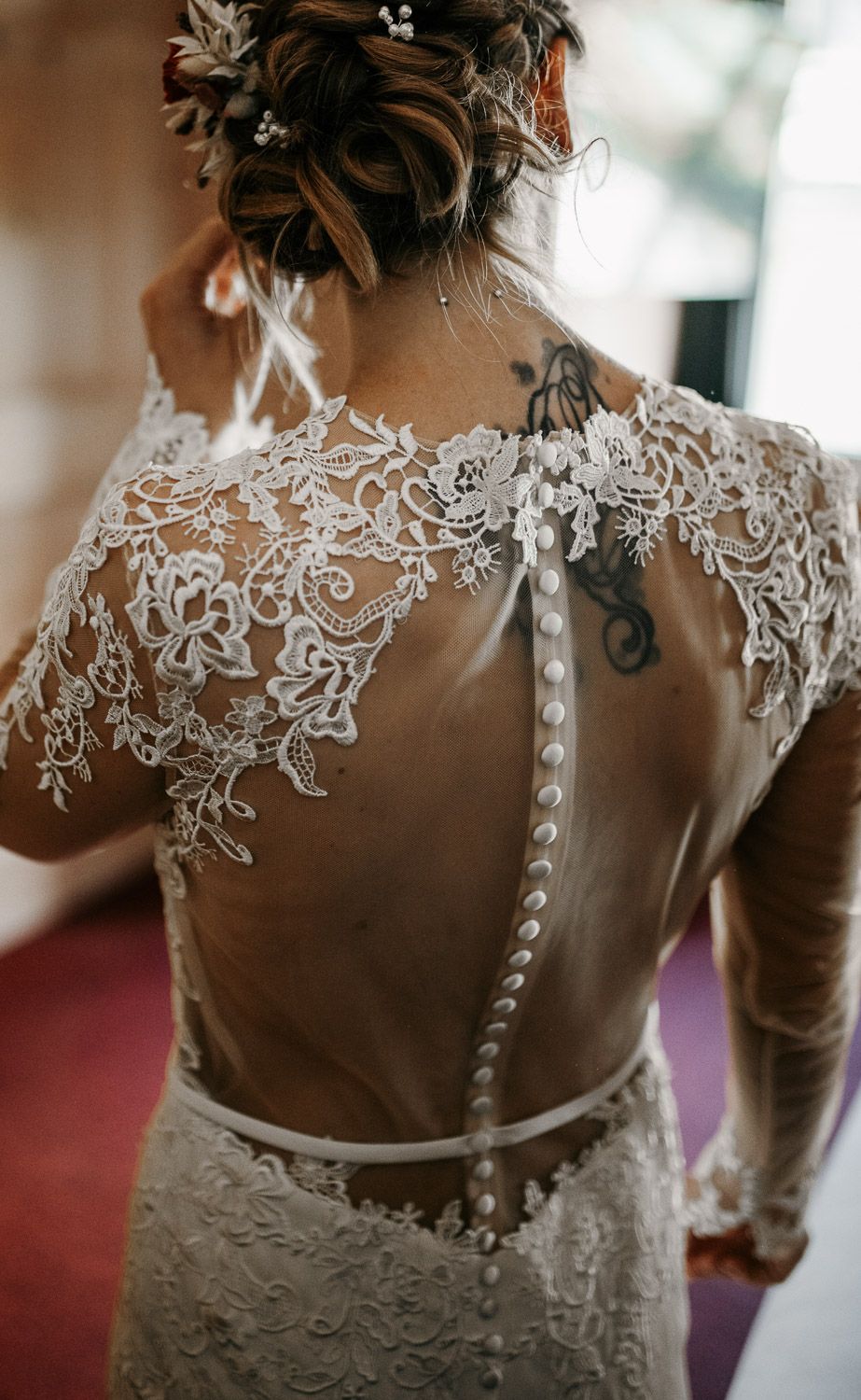 Back view of bride in lace wedding dress with sheer button-up back and floral tattoo detail.