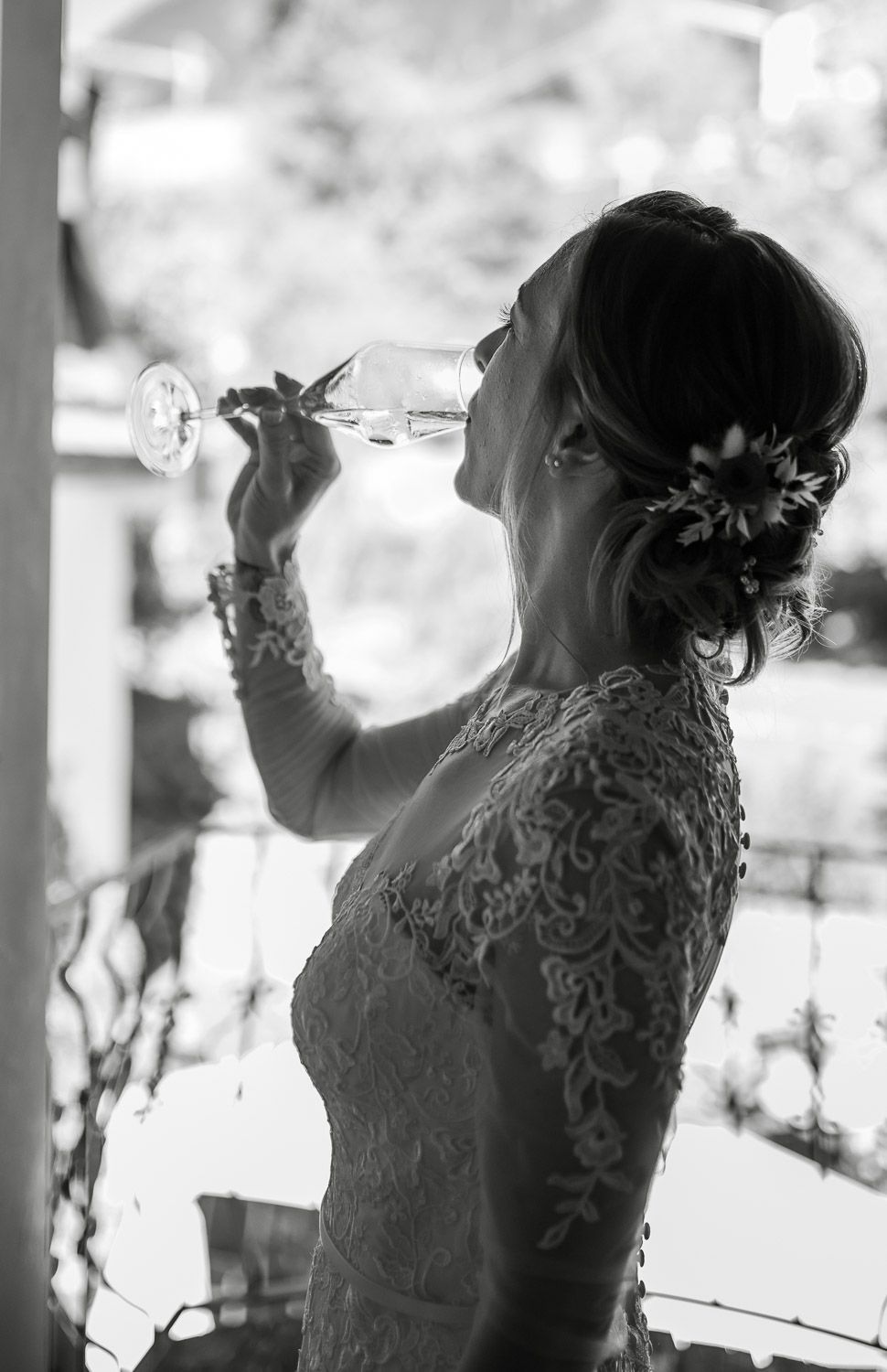 Silhouette of bride in lace gown drinking champagne from a glass in black and white photo.