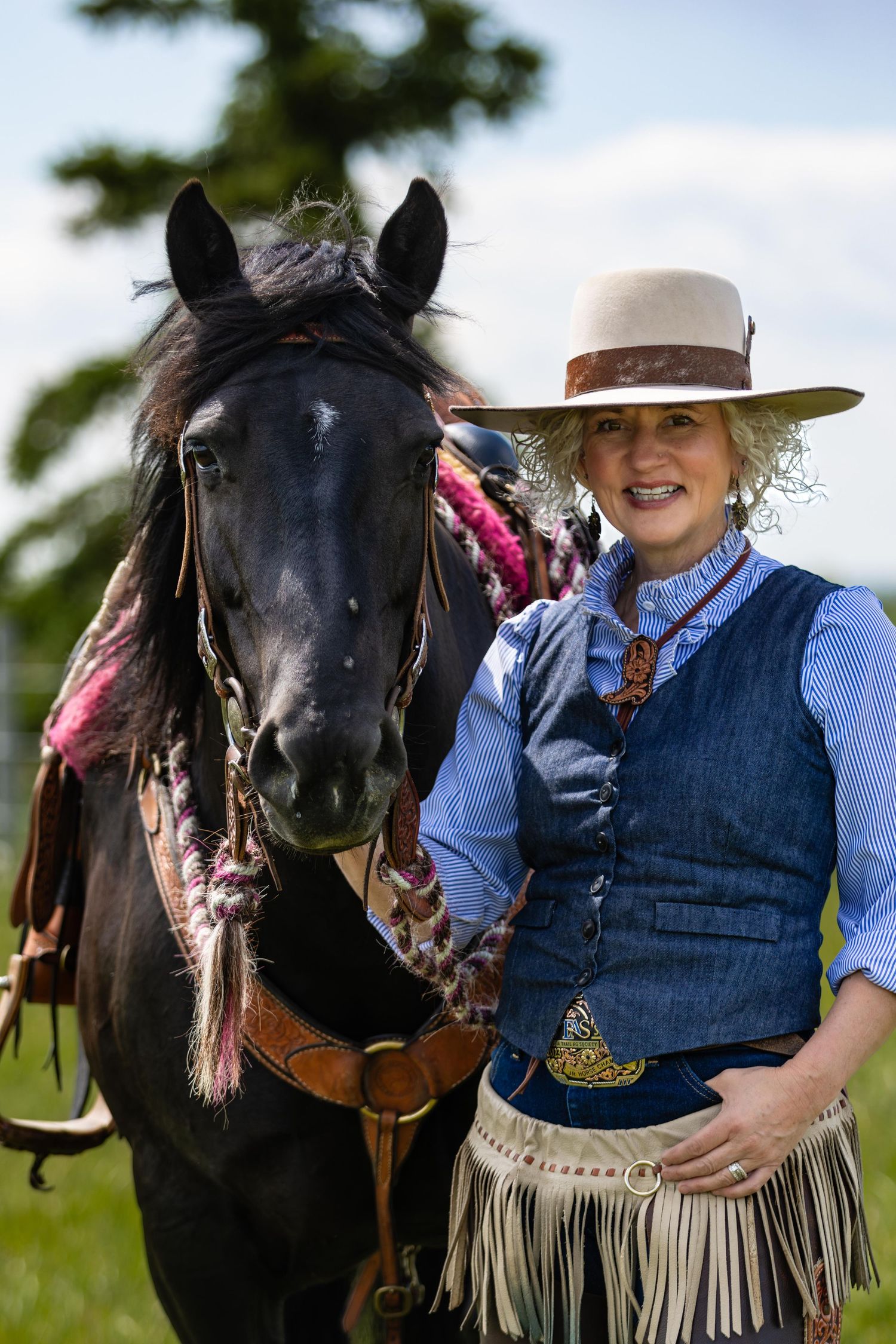 Black horse and western rider in traditional cowboy attire with fringe vest and hat.
