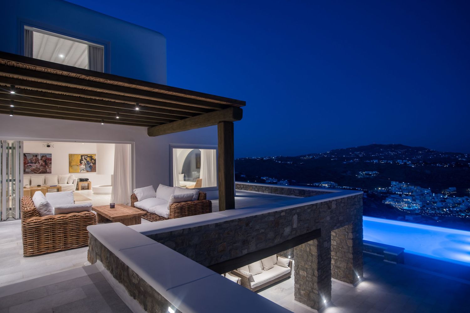 Modern luxury villa with infinity pool and outdoor living space overlooking mountainous landscape at twilight.