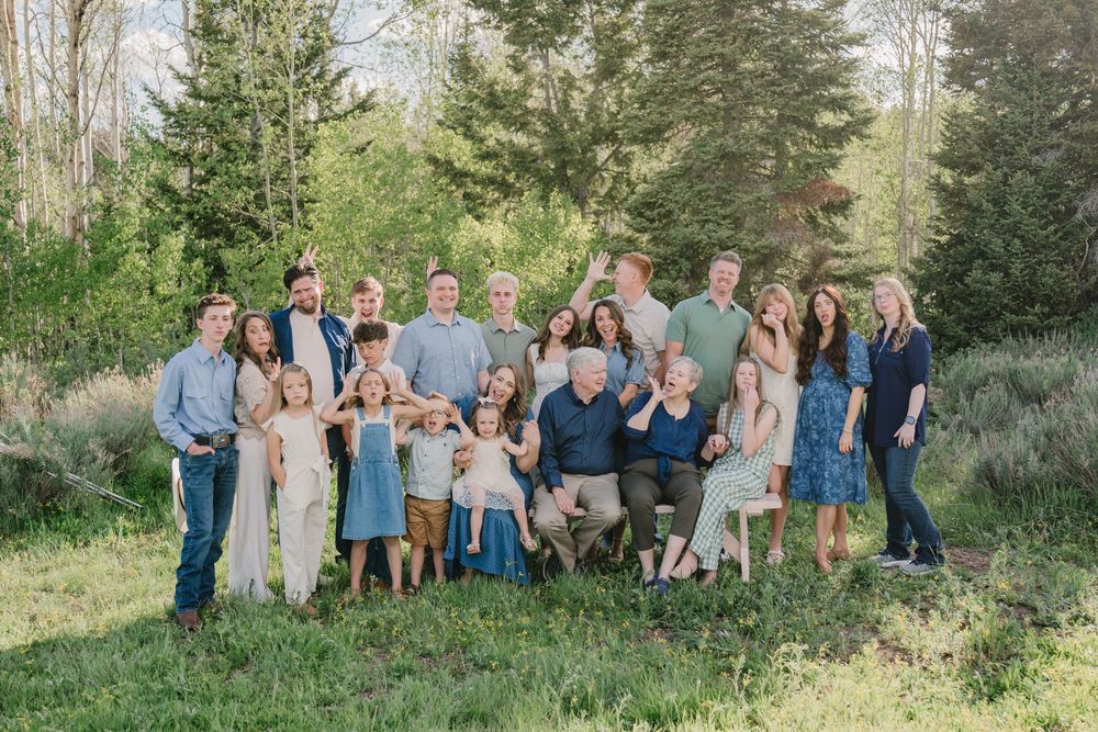 Large extended family posing together outdoors in a lush green setting for a professional portrait photo.