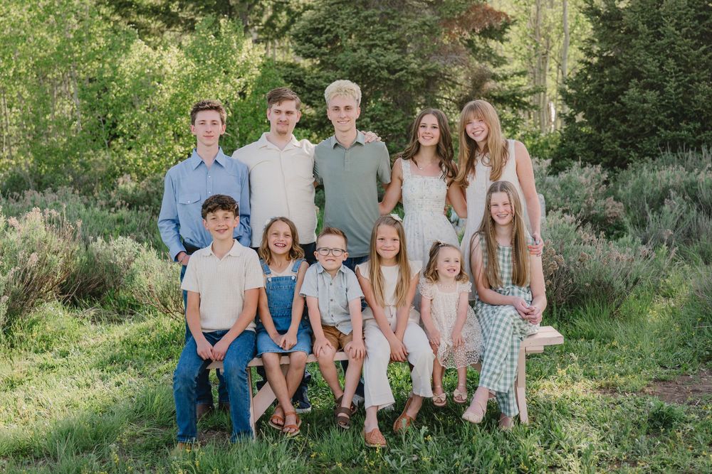 A large family group of ten children posing outdoors in a lush green garden setting for a portrait photo.