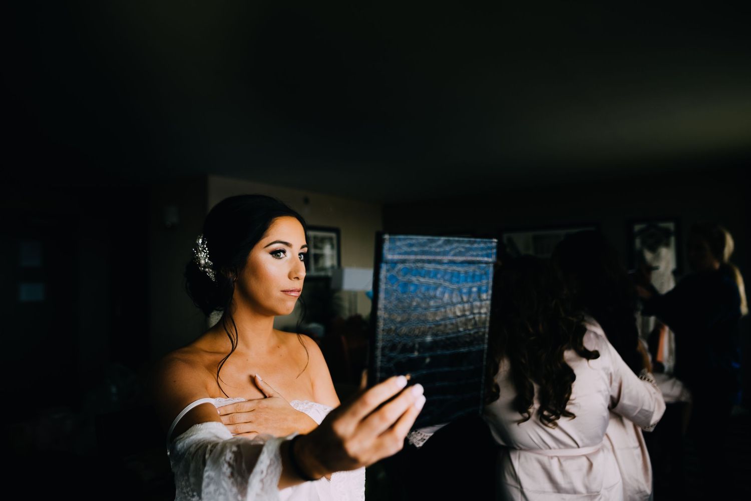 Heather holds up a leather mirror to observe her makeup. She is fixed with diamonds in her hair and a white silk robe.