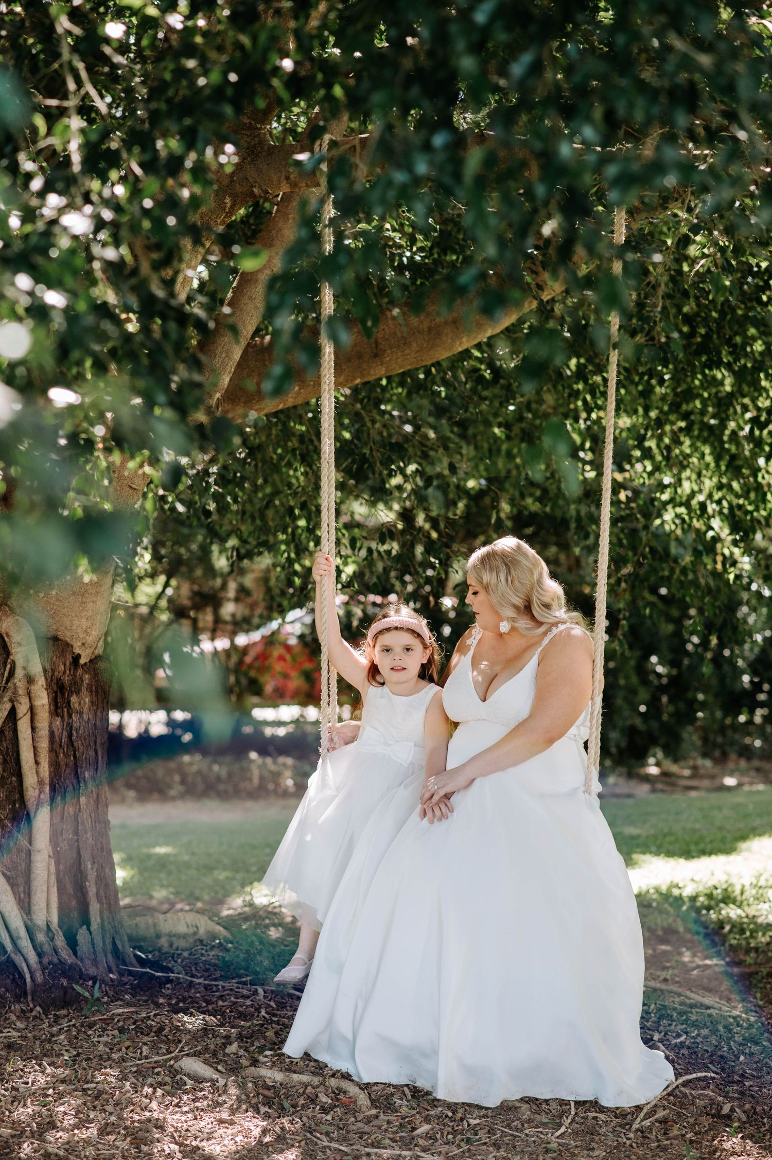 Two people in white dresses sharing a moment on a garden swing.