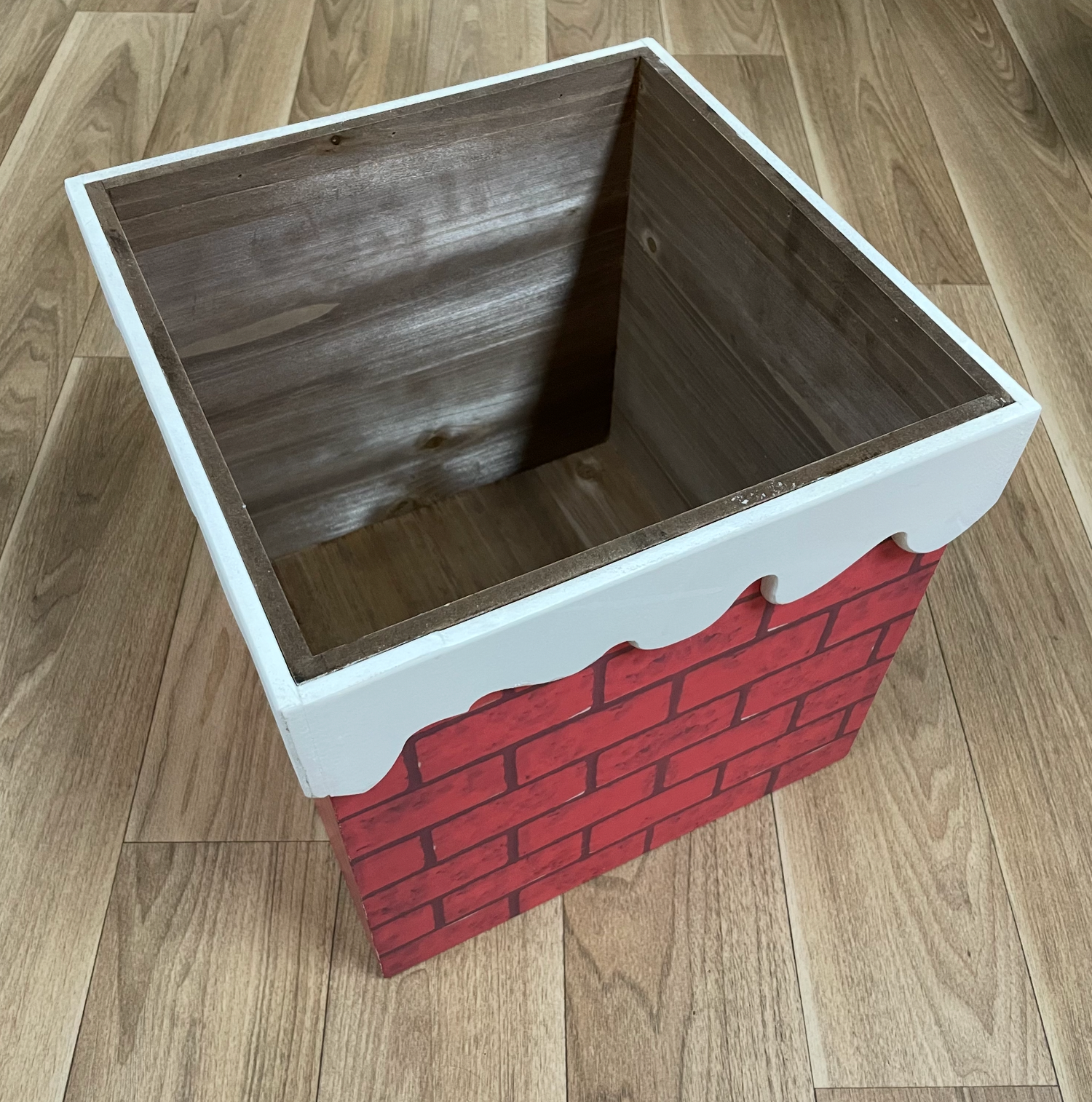 DIY wooden box with red brick pattern painted on the side showing assembly progress.