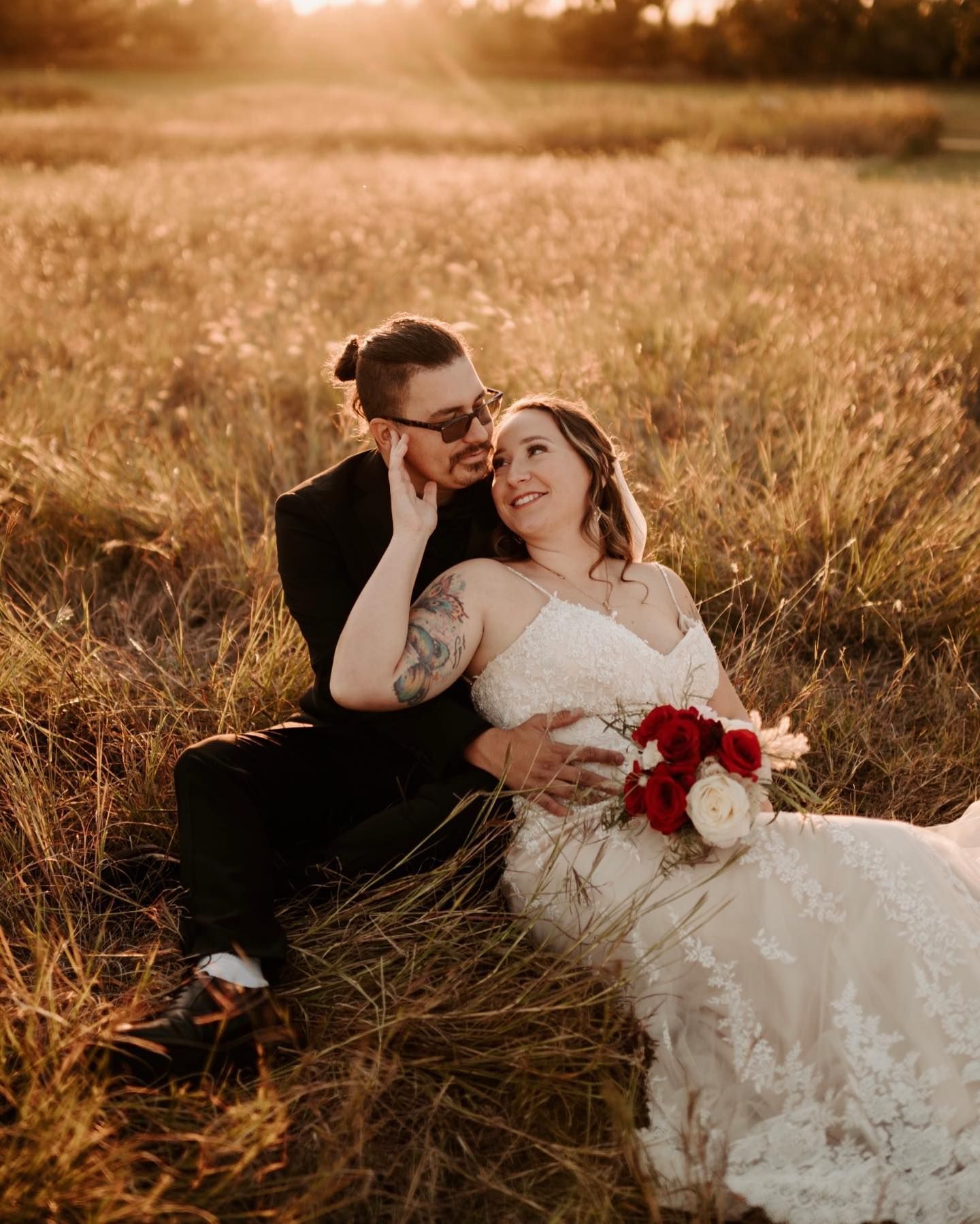 Wedding couple sits together in golden sunlit field of tall grass. Oklahoma Wedding Photographer