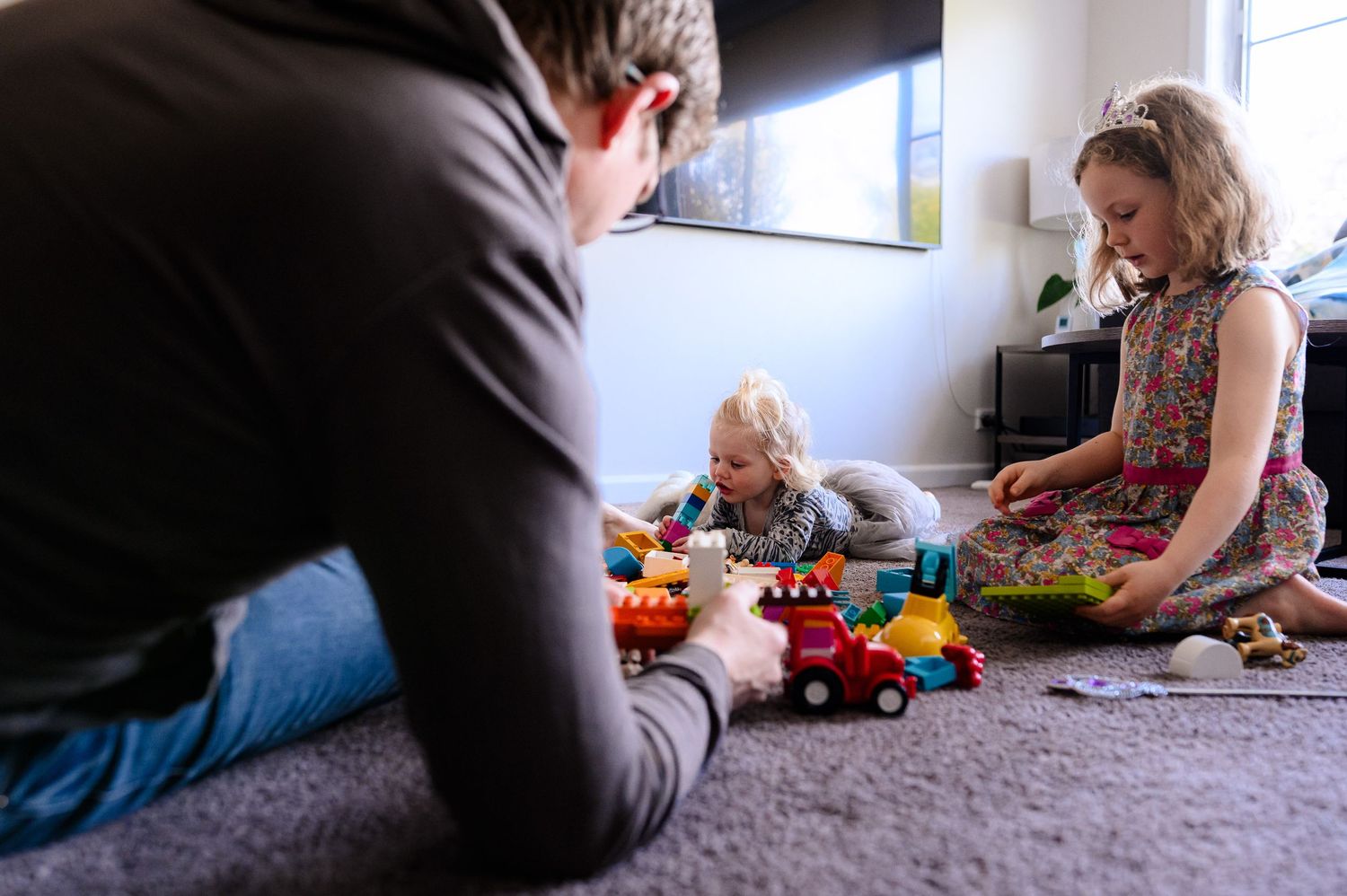 A family playing with toys together on a carpeted floor.