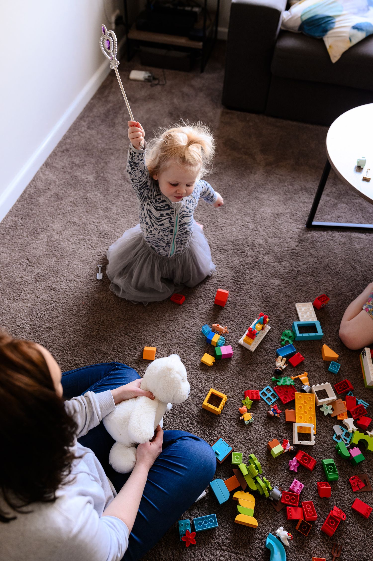 Child in a grey dress plays with colorful building blocks while others join in.