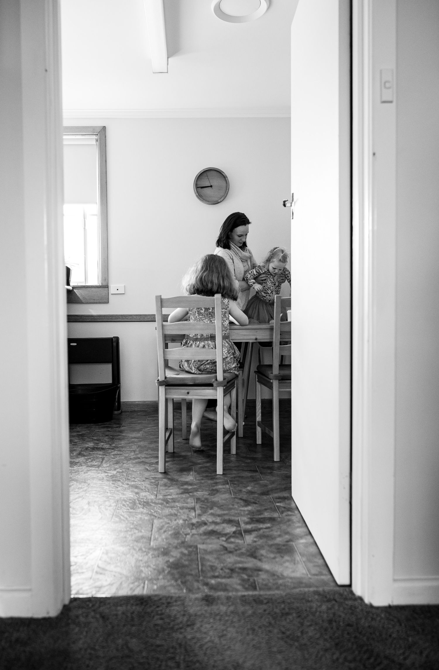 Black and white photo showing family time in a dining room through a doorway.