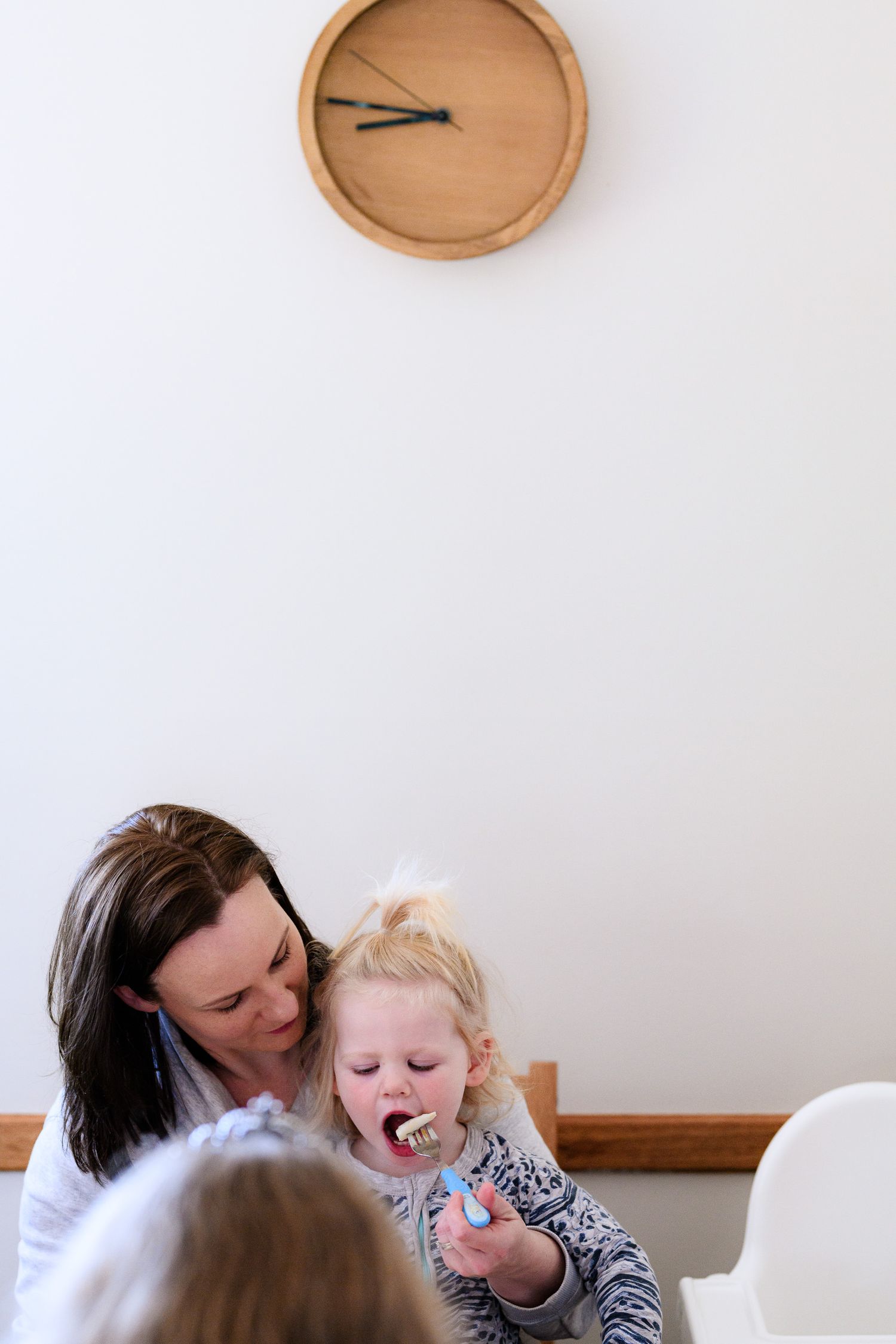 Intimate family moment under a minimalist wooden wall clock.