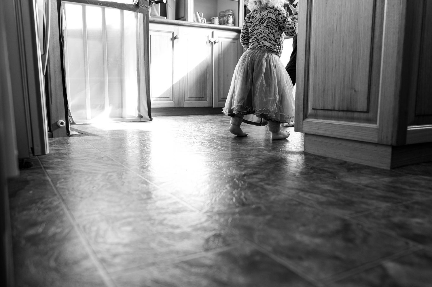 Low angle black and white shot of small legs standing on kitchen floor.