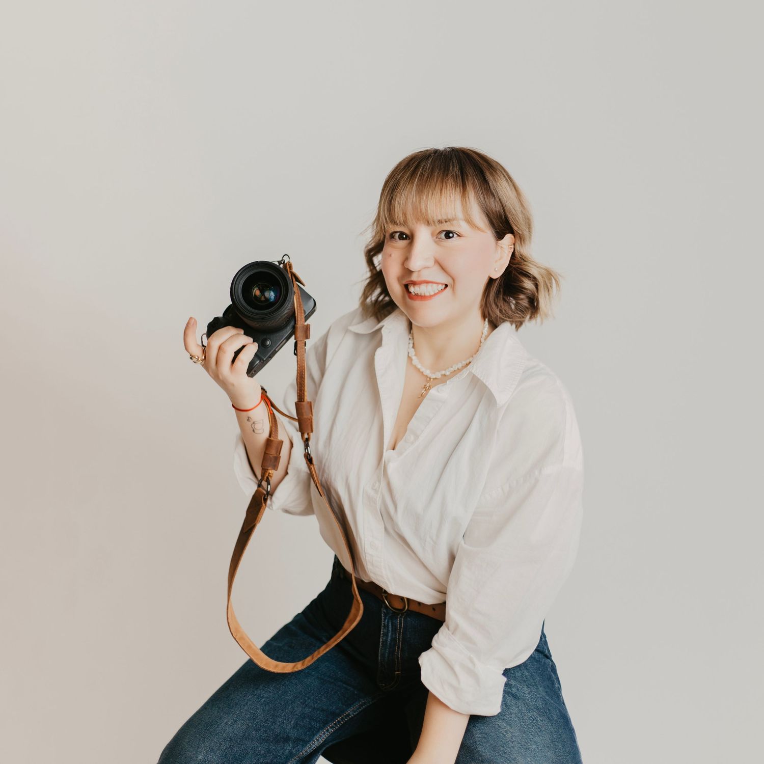Professional photographer poses with vintage camera in casual white shirt and jeans.