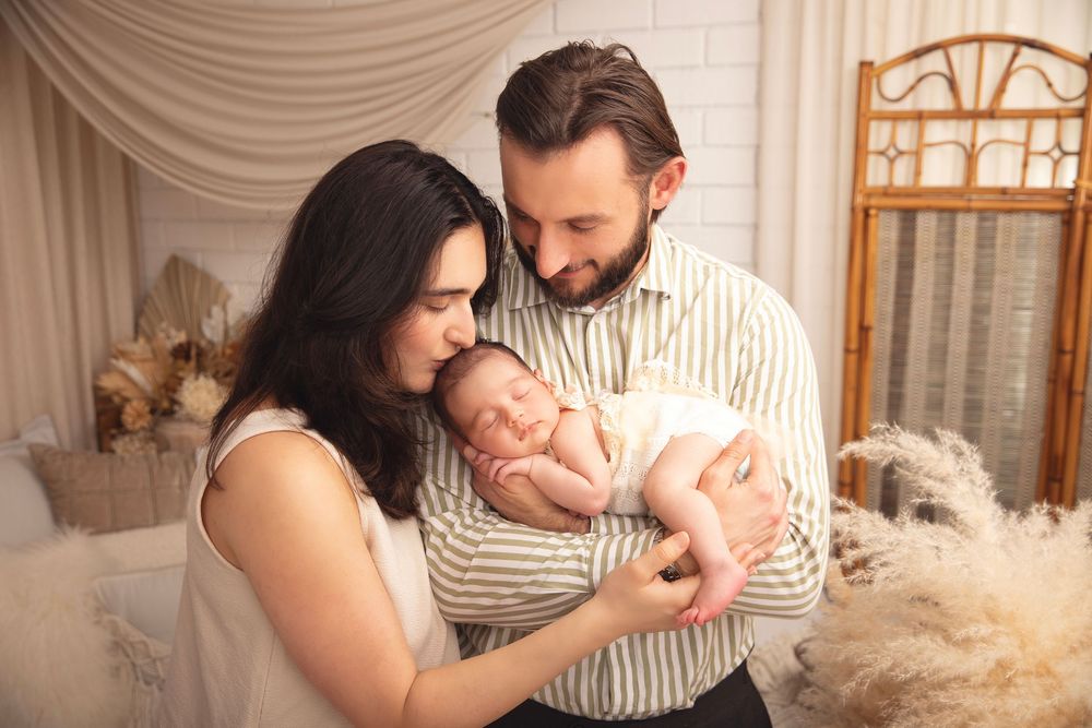 Happy parents tenderly hold their sleeping newborn baby during a warm studio family photo session.