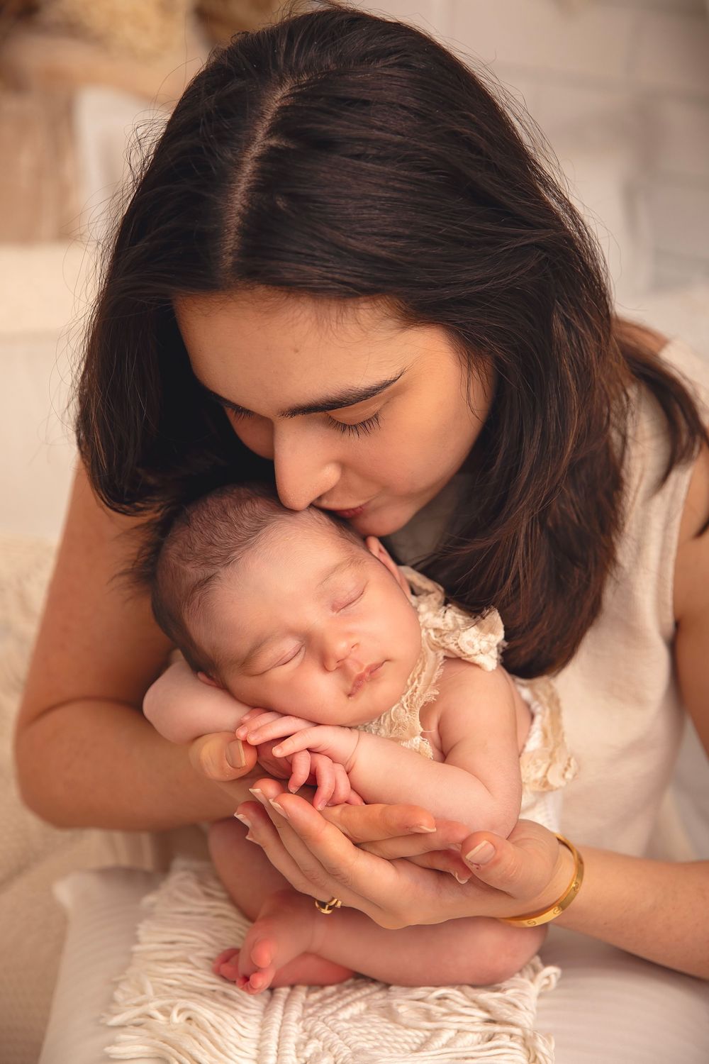 Loving mother gently kisses sleeping newborn baby during intimate studio newborn photography session.