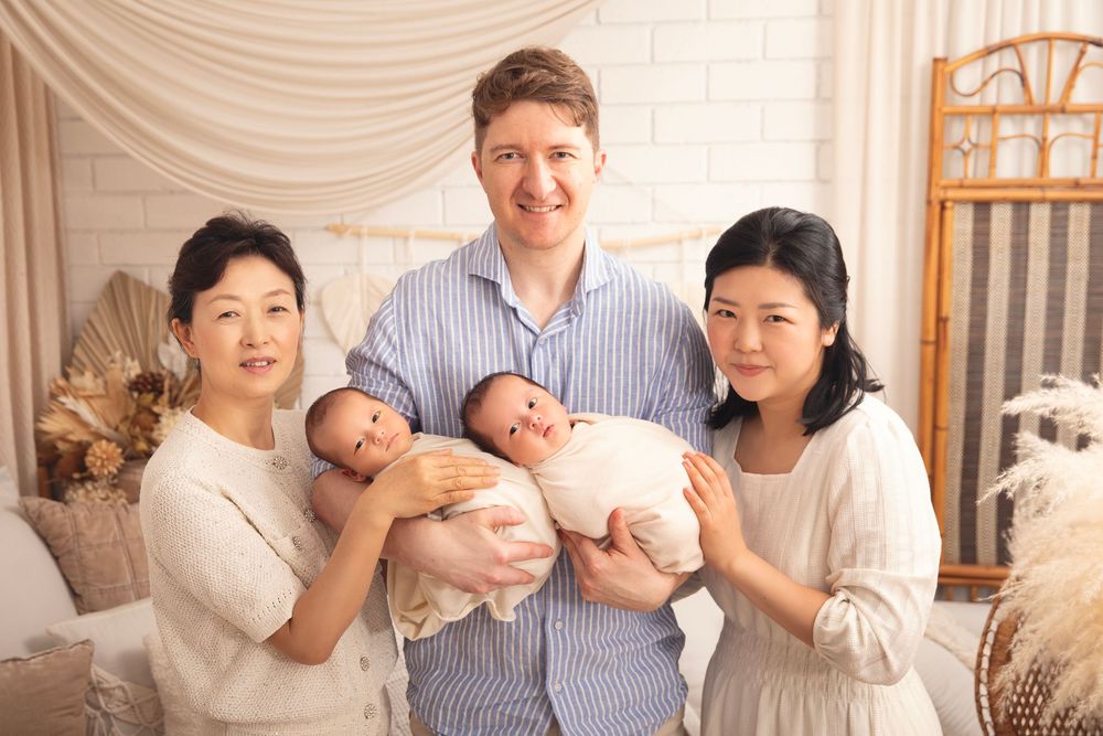 Family photo of two women holding newborn twins with a man in a softly decorated studio setting.