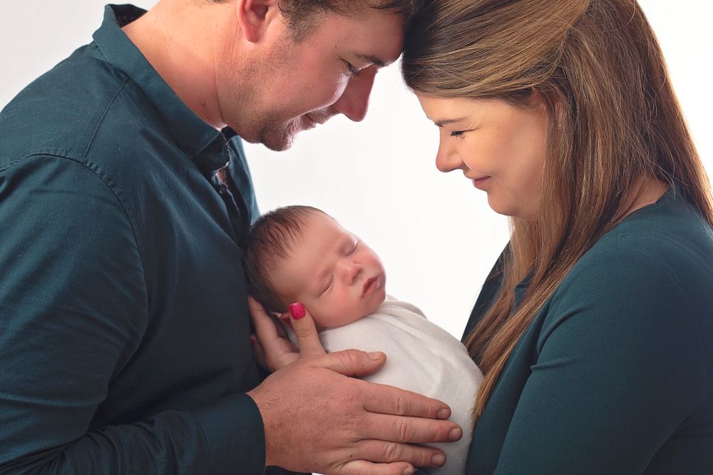 Loving parents cradling their swaddled newborn baby during professional newborn photography session.
