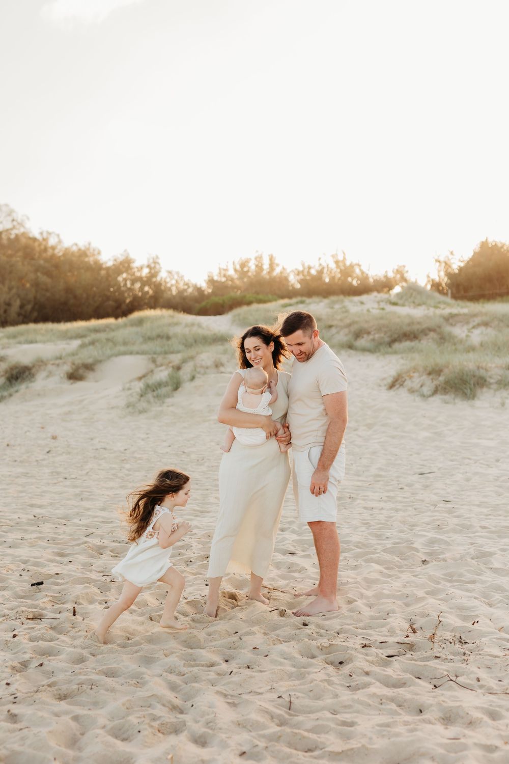 A candid photo of a girl running around her parents and little sister on the beach in the Sunshine Coast. Dad and mum are watching on.