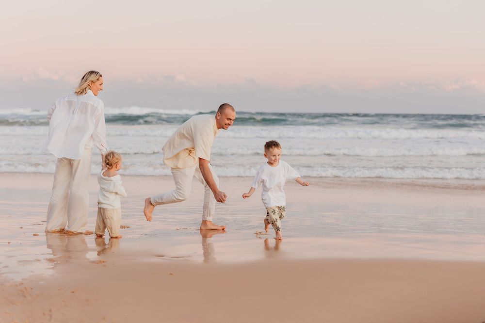 Dad chasing boy across the sandy beach at sunset with fairy floss skies in the background and the waves and ocean.