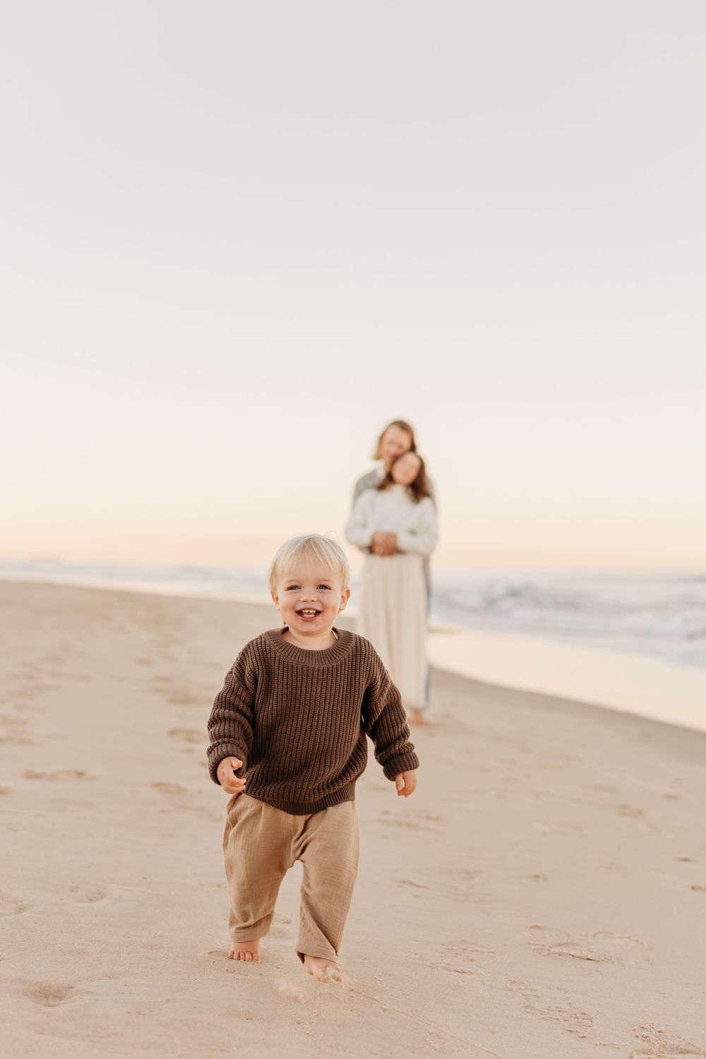 A boy running in front of mum and dad towards the camera at sunset golden hour family photography session.