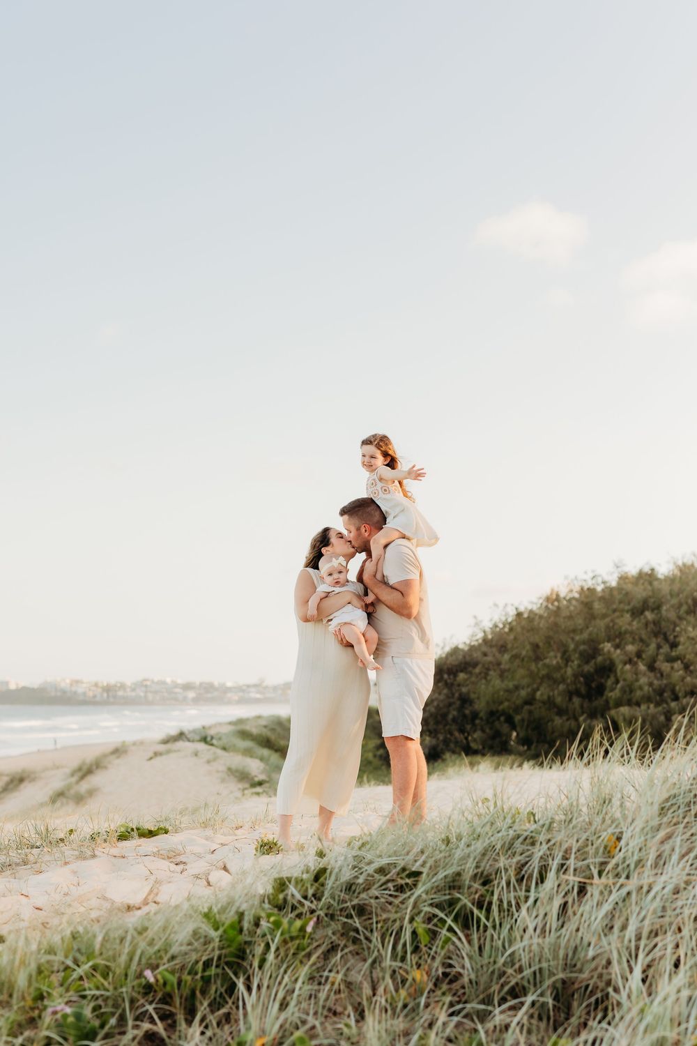 Mum and dad and two girls, dad holding little girl up on shoulders. Relaxed family session on the Sunshine Coast while on Holidays.