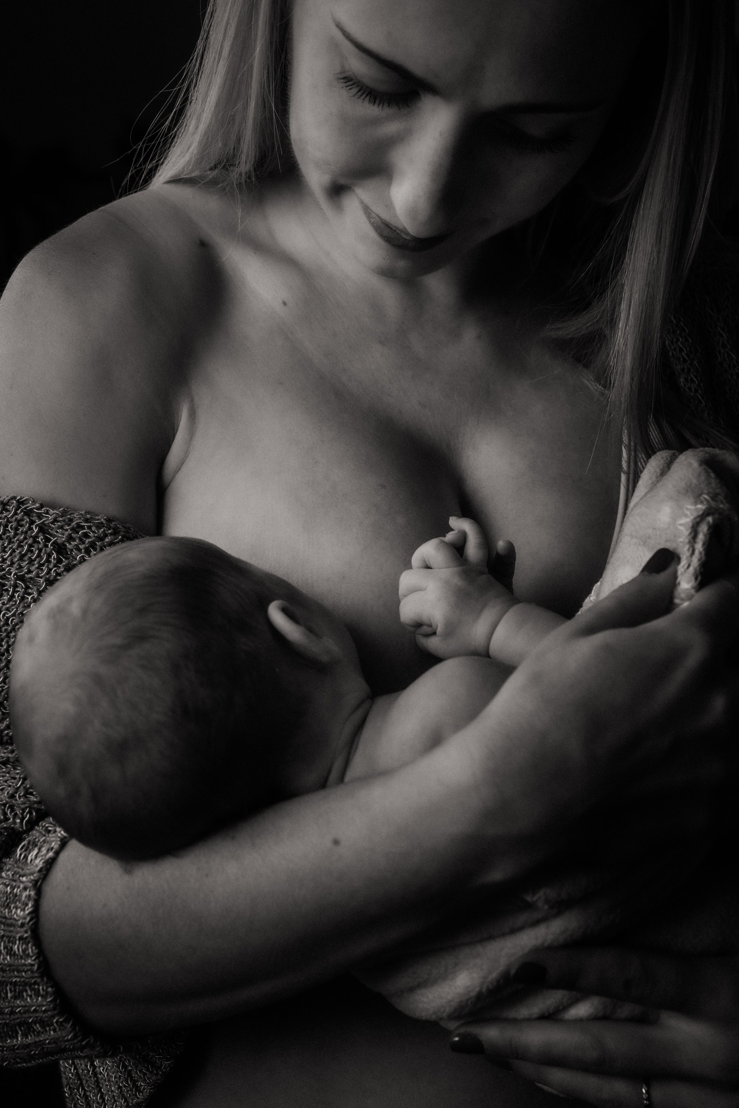 An intimate black and white portrait capturing a tender moment of motherhood and breastfeeding.