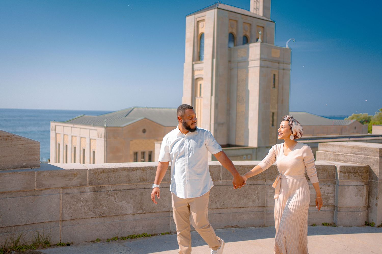 Couple in white outfits poses at a Mediterranean architectural location with white buildings.