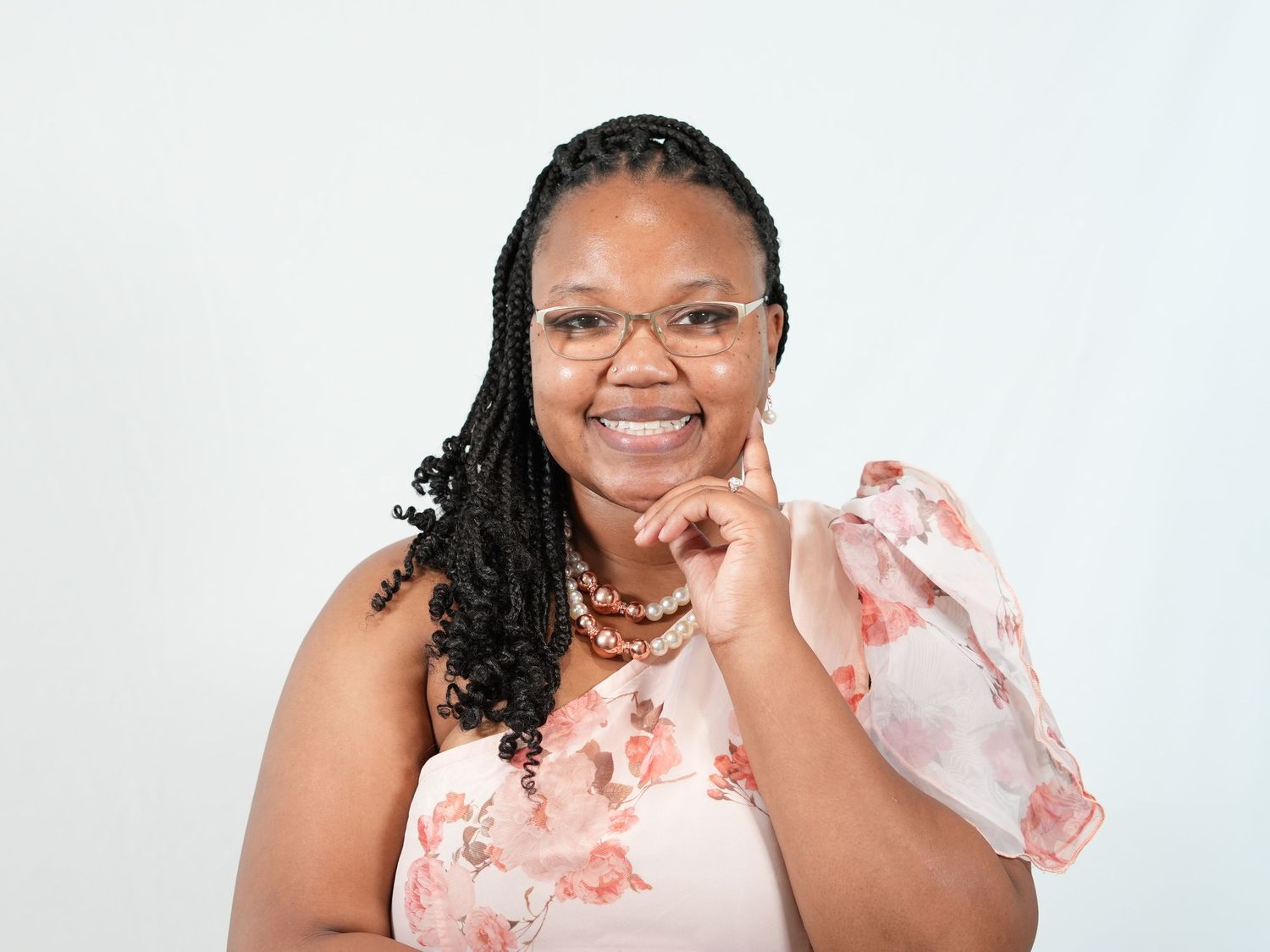 Professional headshot of someone wearing a floral dress and beaded necklace against white background.