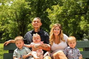 Mom and dad with their kids smiling on a bench at stockstill park in front of trees.