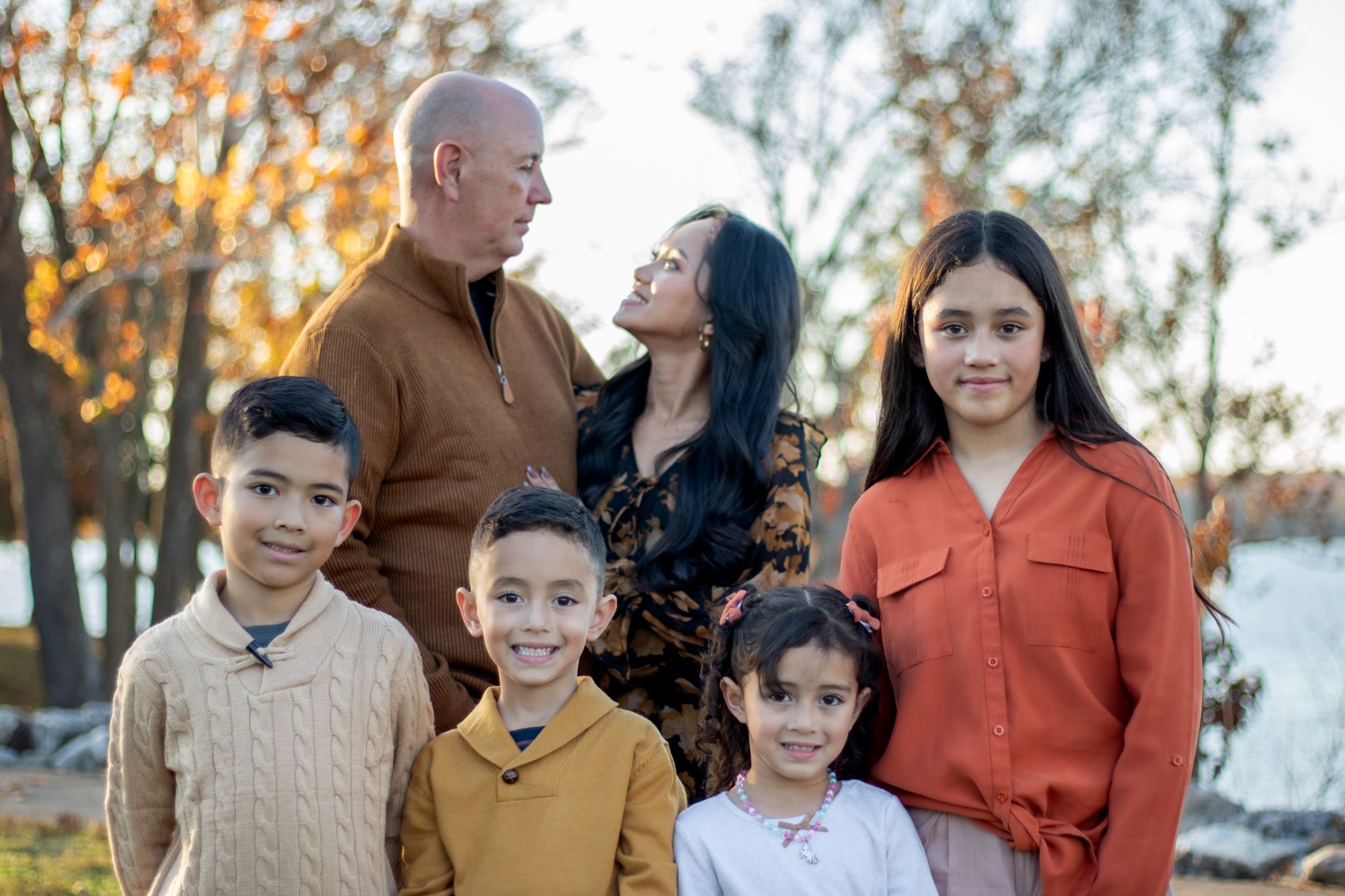 Parents looking at each other with their kids in front of them smiling at the camera.