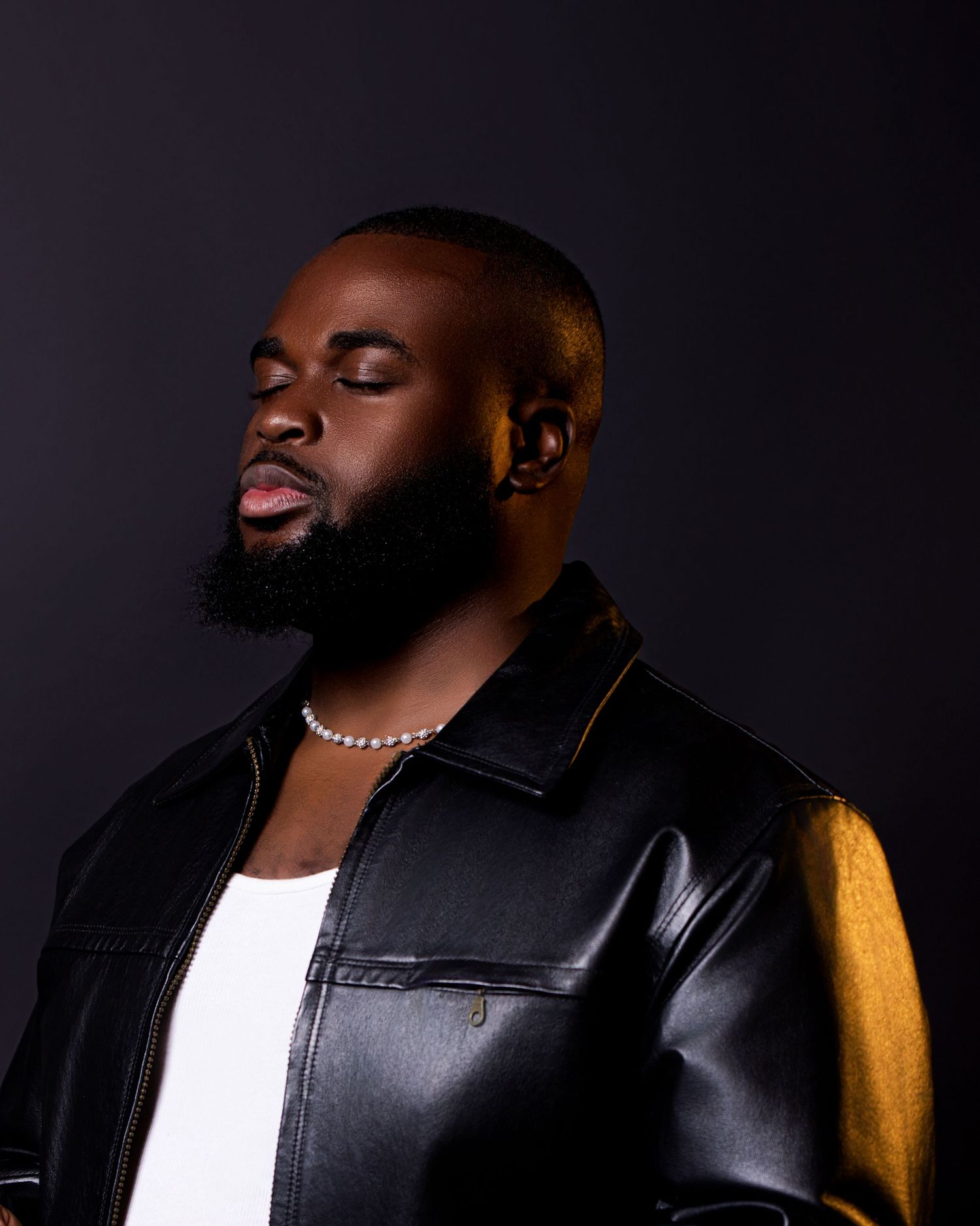 Artistic portrait of man in leather jacket against dark background with dramatic lighting.
