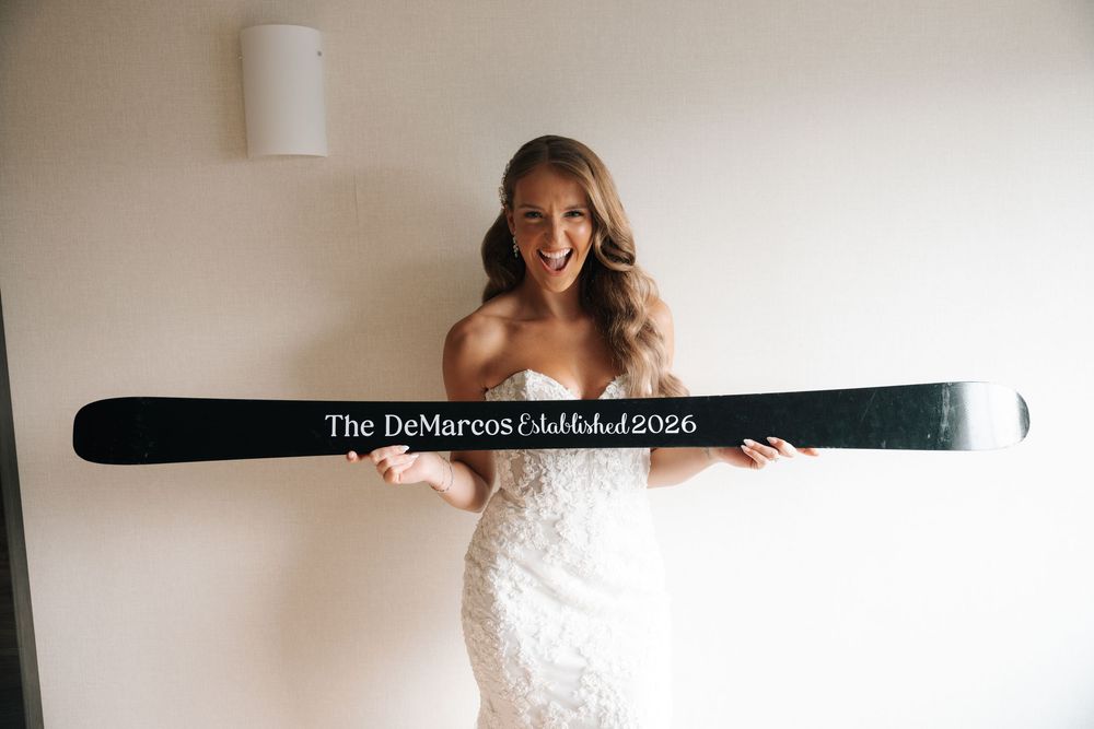 Bride in strapless lace gown holds a custom ski inscribed with The DeMarcos Established 2026.