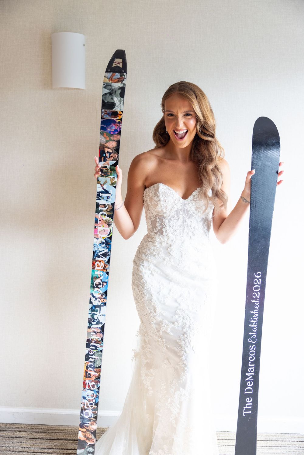 Excited bride in lace wedding dress holds two custom skis, one decorated with colorful graphics.