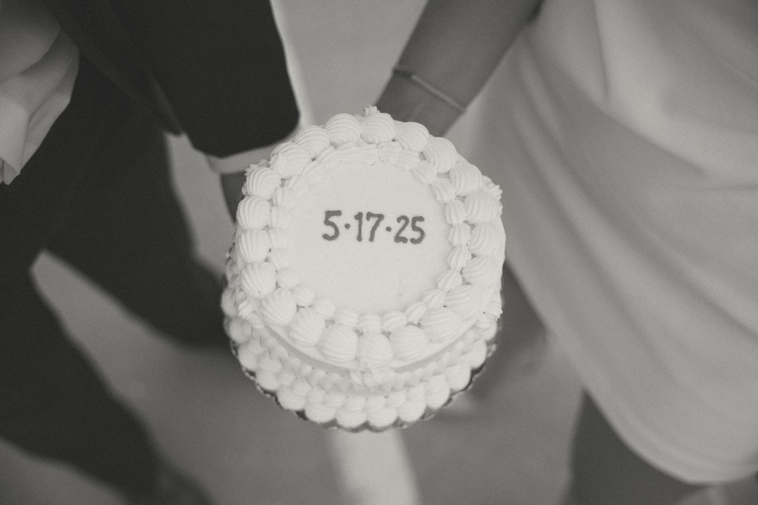 A white frosted cake with the date 5-17-25 written on top in a minimalist style.
