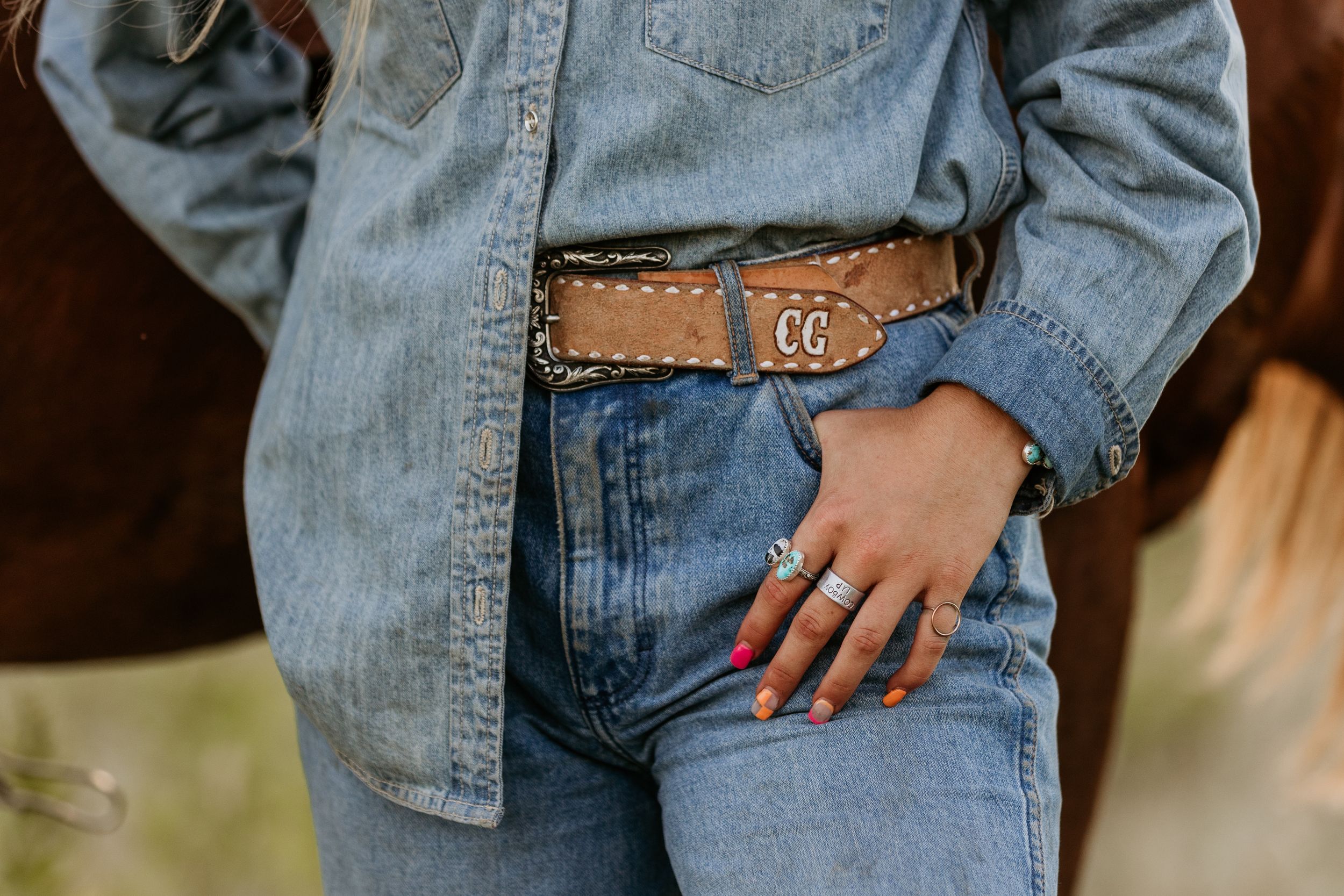 Cowgirl wearing double denim outfit with a brown leather belt featuring a decorative buckle detail.