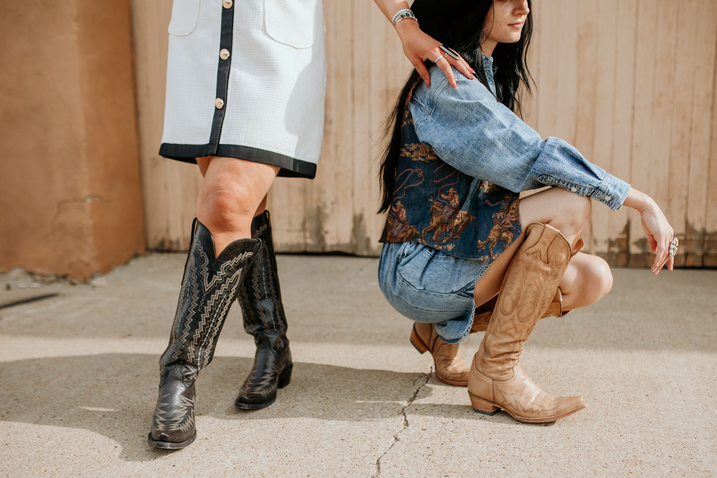 Two people showcase western-style cowboy boots while wearing denim on a concrete surface.