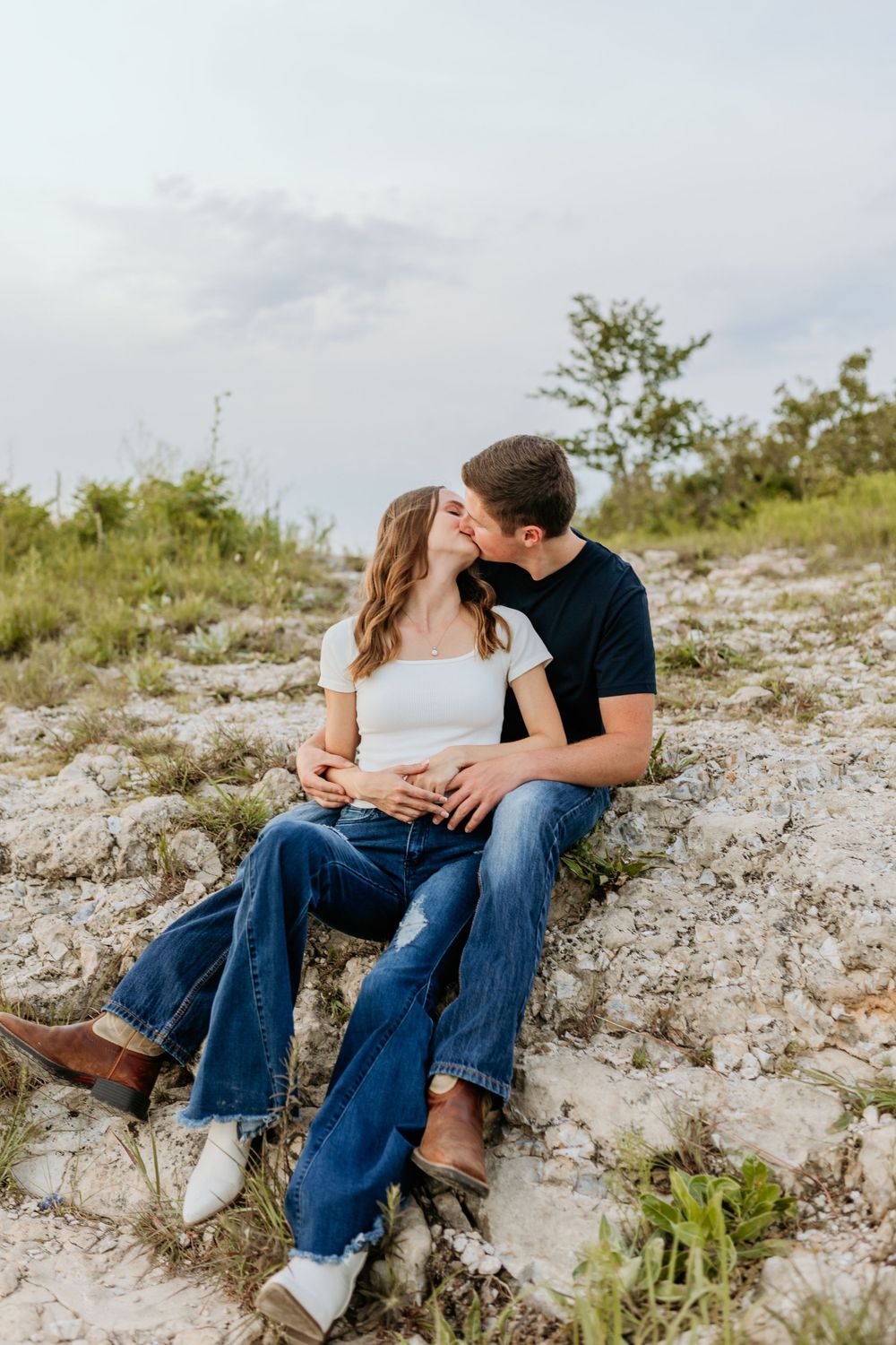 A couple share an intimate moment together while sitting on rocky terrain during golden hour.