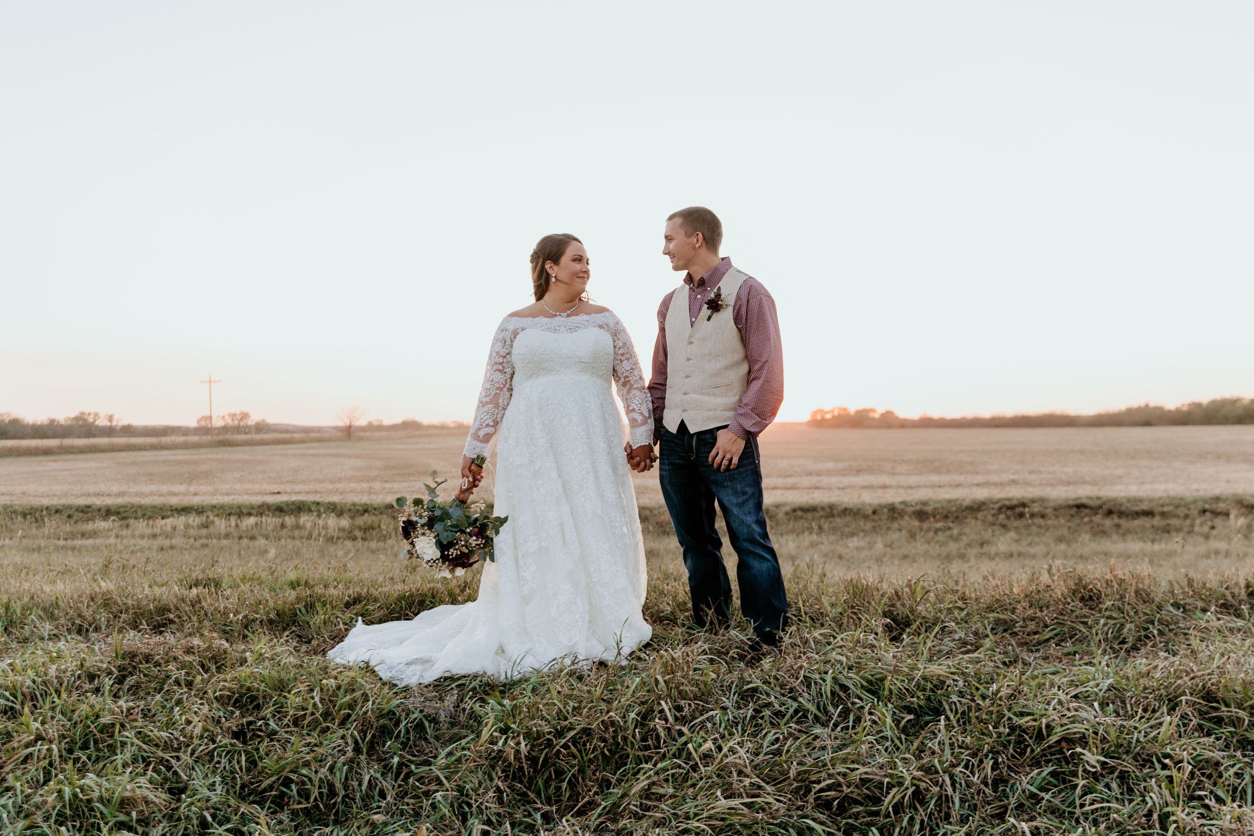 A couple shares a romantic moment in formalwear while standing in a field at sunset.