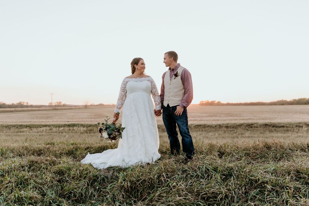 A couple shares a romantic moment in formalwear while standing in a field at sunset.