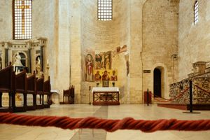 Simple church altar area with wooden pews and colorful religious artwork on stone walls.