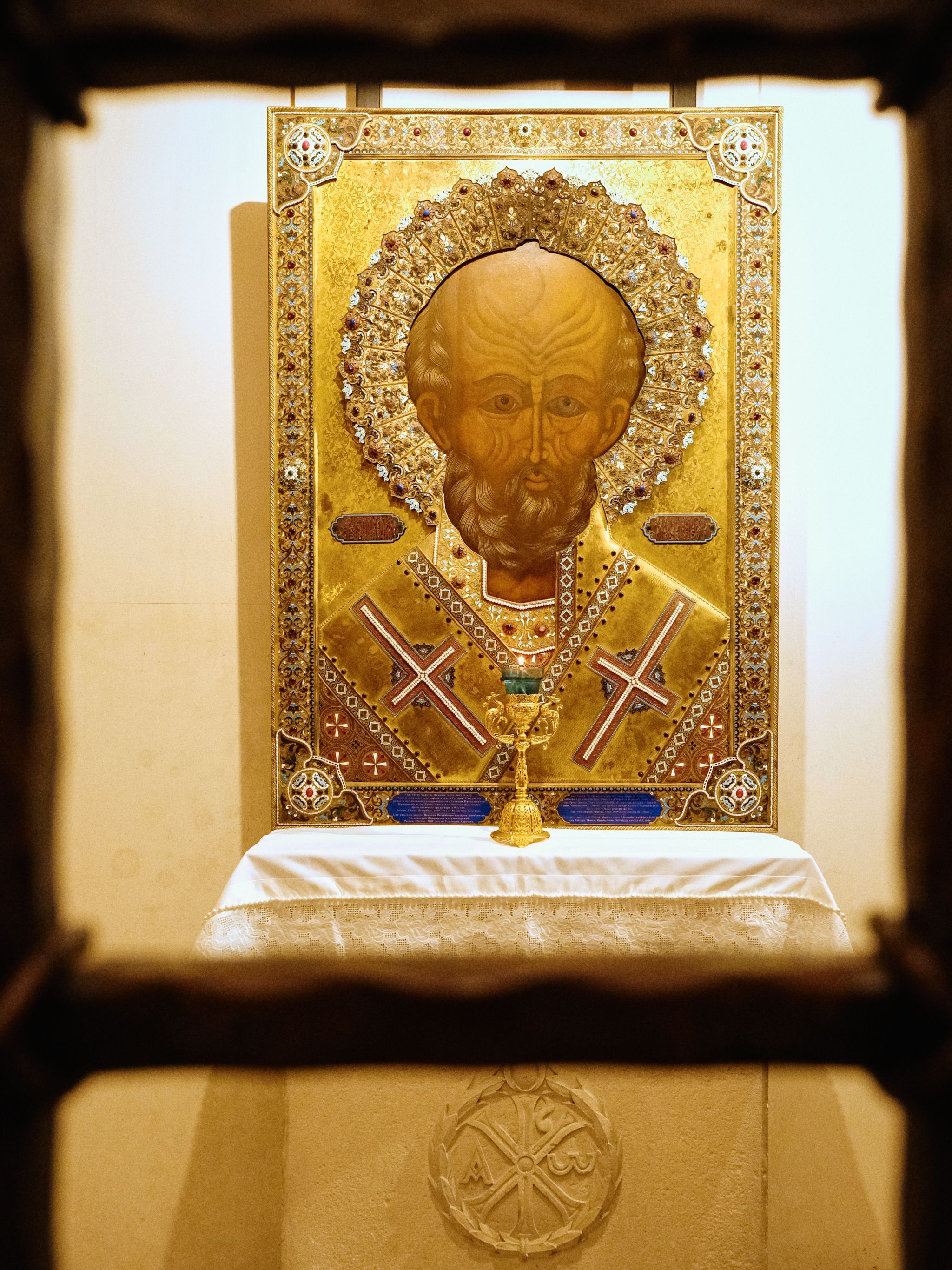 Orthodox religious icon with golden ornate frame displayed in a church setting.