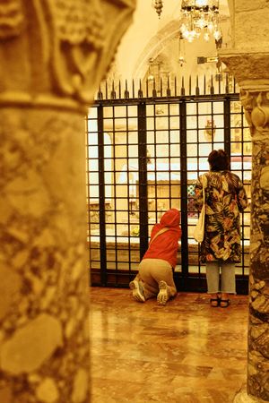 People praying at an ornate church gate with golden interior architectural details.