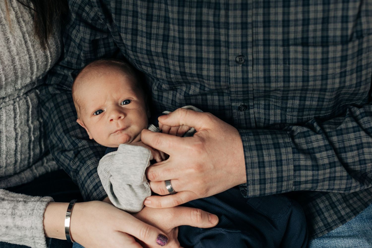 Close-up of tiny baby being held in adult hands against plaid fabric.