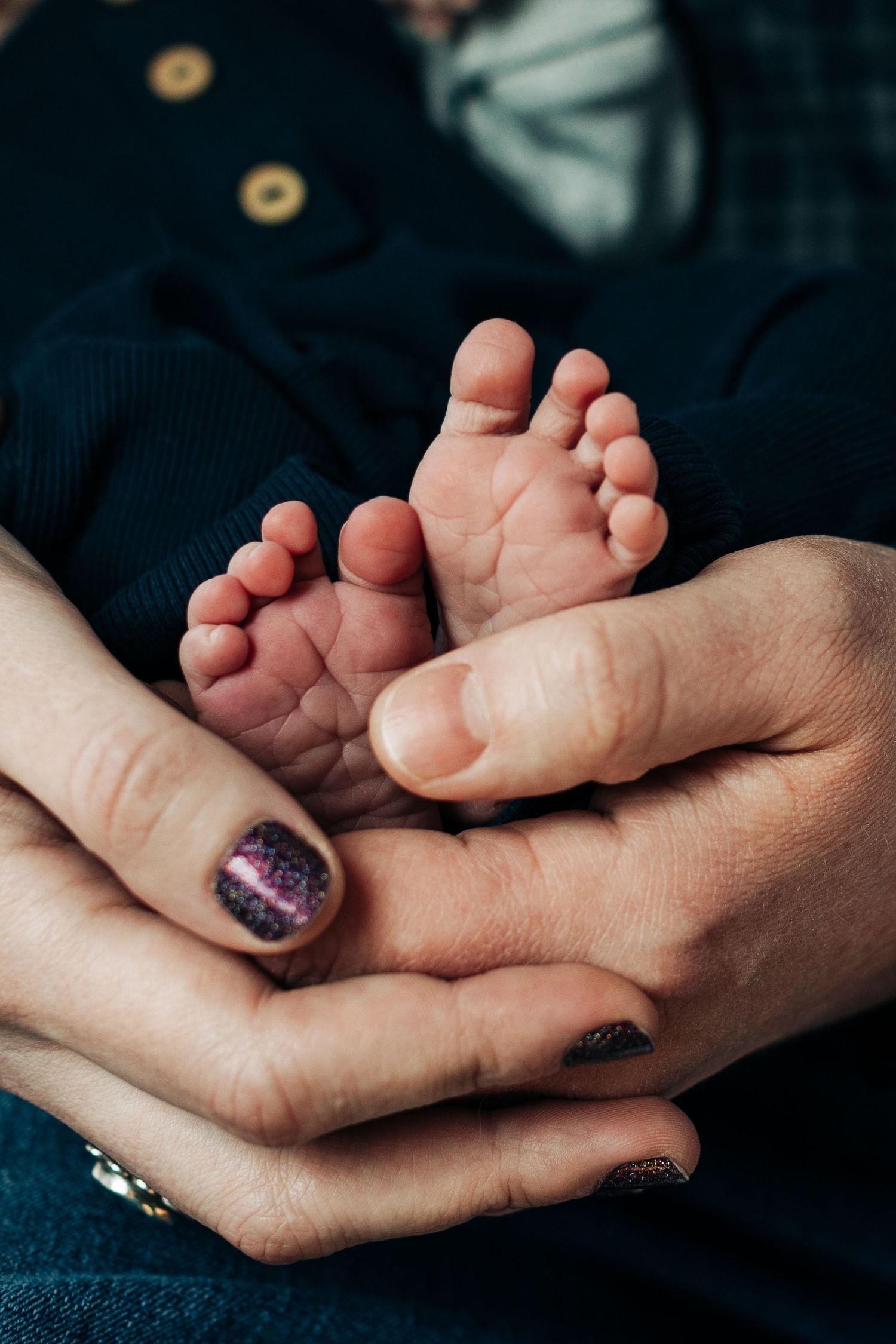 Close-up of tiny baby feet being held in hands with sparkly nail polish.