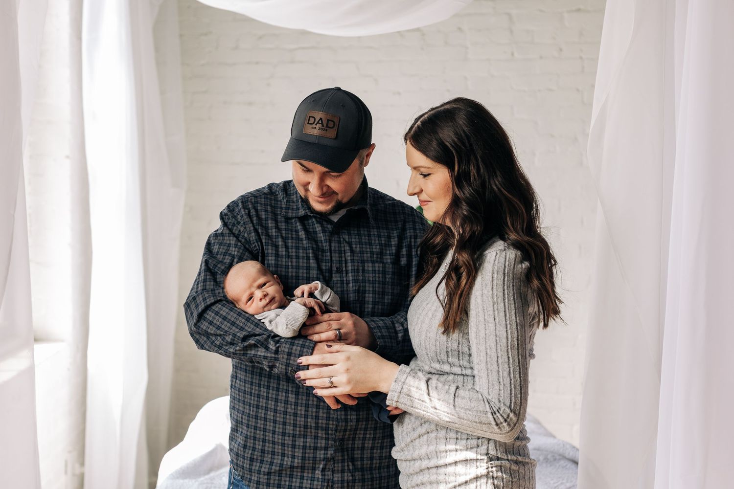 Parents sharing a tender moment with their newborn baby against a white backdrop.