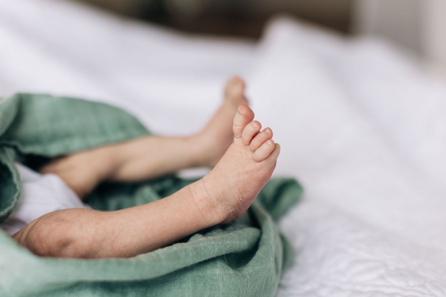 Close-up of tiny baby feet peeking out from mint green fabric against white bedding.