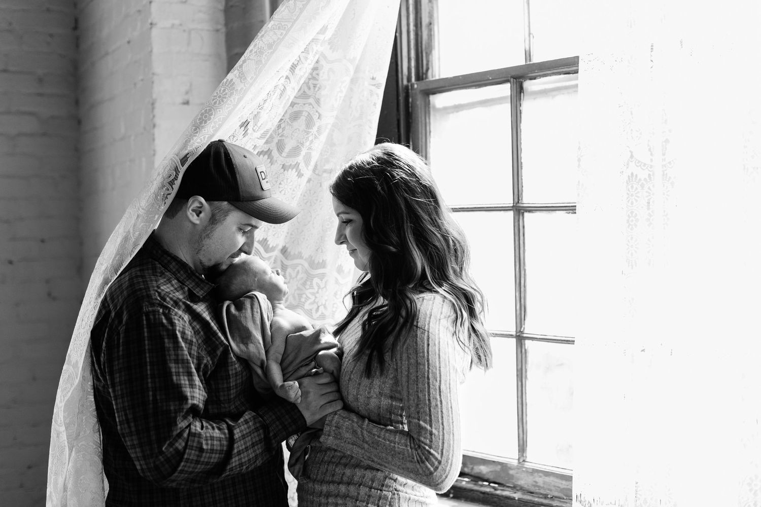 A couple shares an intimate black and white moment by a window.