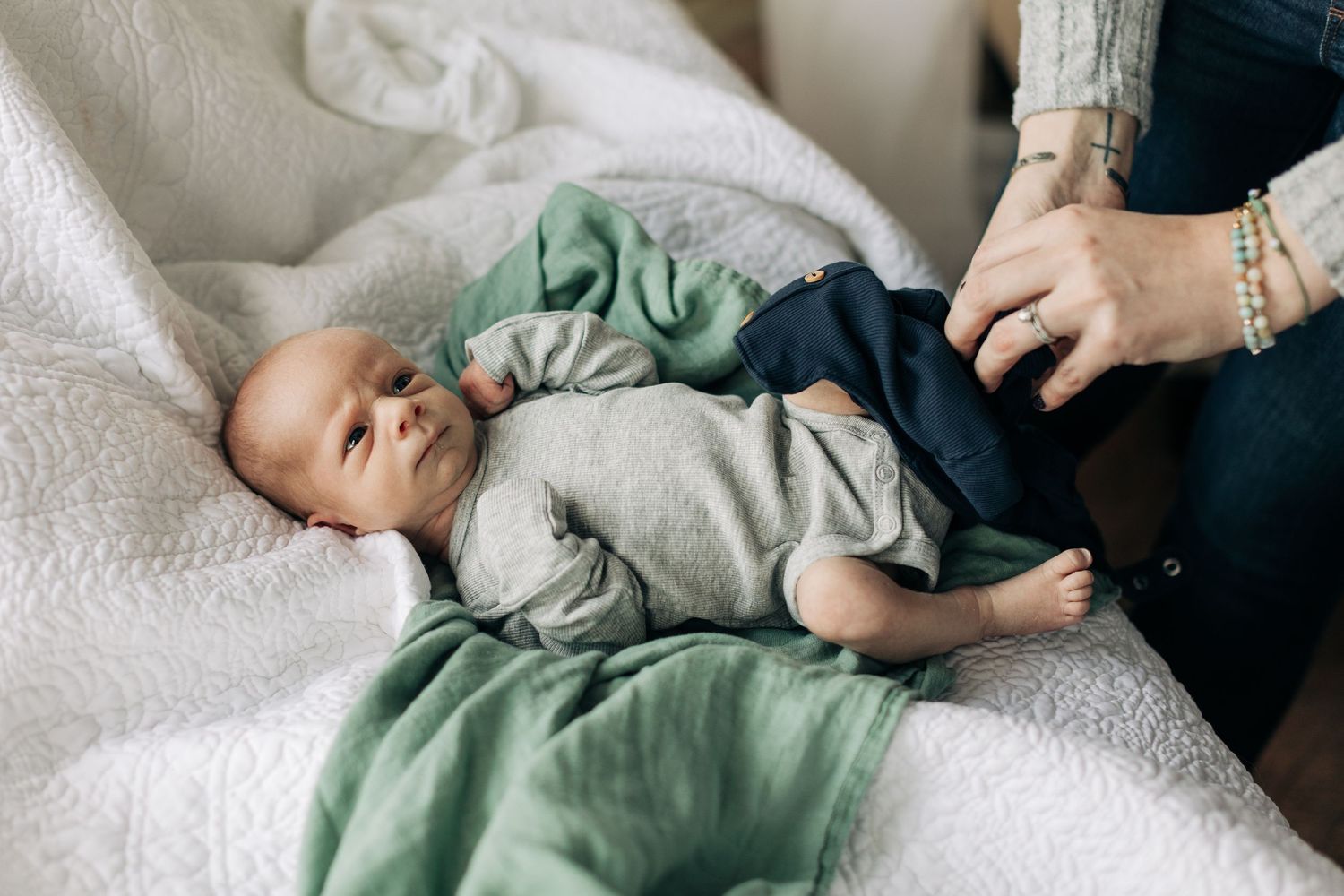 A newborn baby in gray and navy clothing lies contentedly on white bedding.